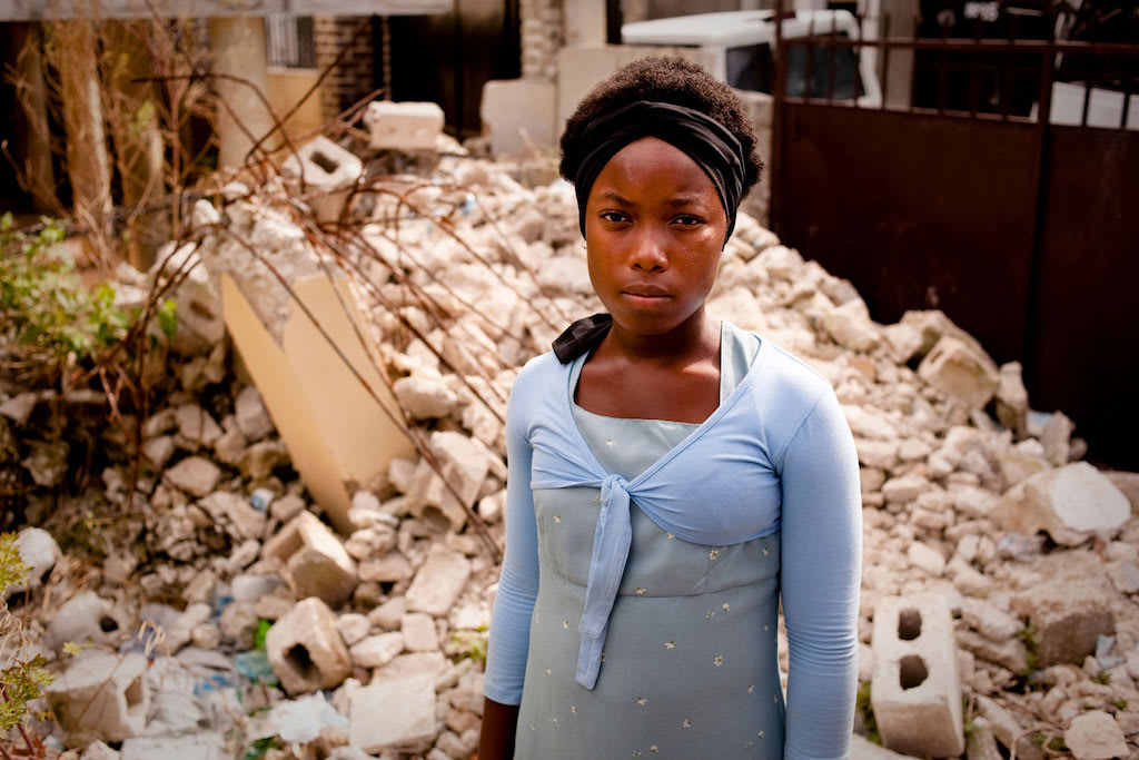 A Haitian teenager stands in the rubble of a building.